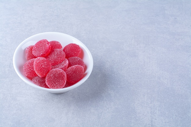 회색 배경에 빨간색 설탕 과일 젤리 사탕으로 가득 찬 흰색 깊은 접시. 고품질 사진