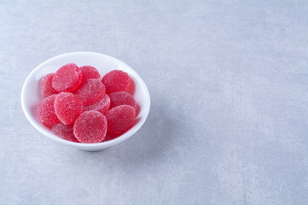 A white deep plate full of red sugary fruit jelly candies on gray background. High quality photo