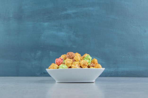 A white deep plate of sweet multicolored popcorn . 