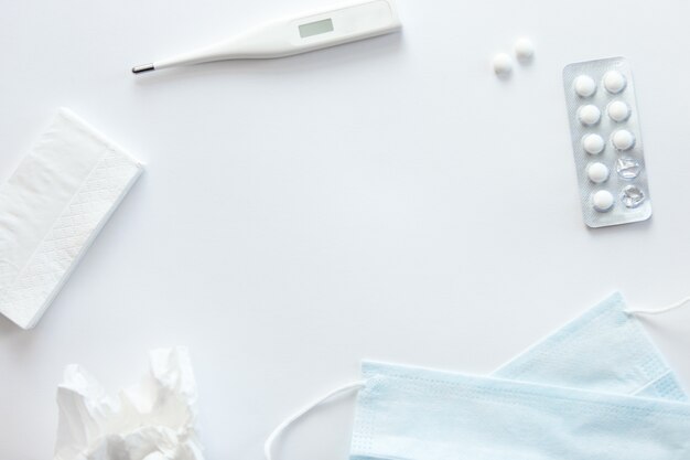 White desk with round pills, thermometer, napkin, medicine mask