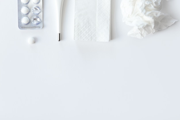 White desk with round pills, thermometer, paper crumpled napkin