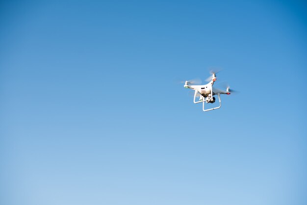 Белый беспилотник летит в небе, записывая видео