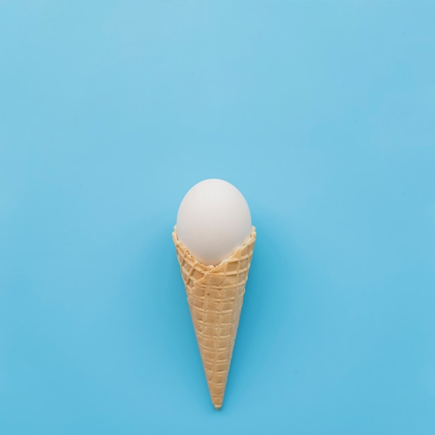 White egg in waffle horn on blue background