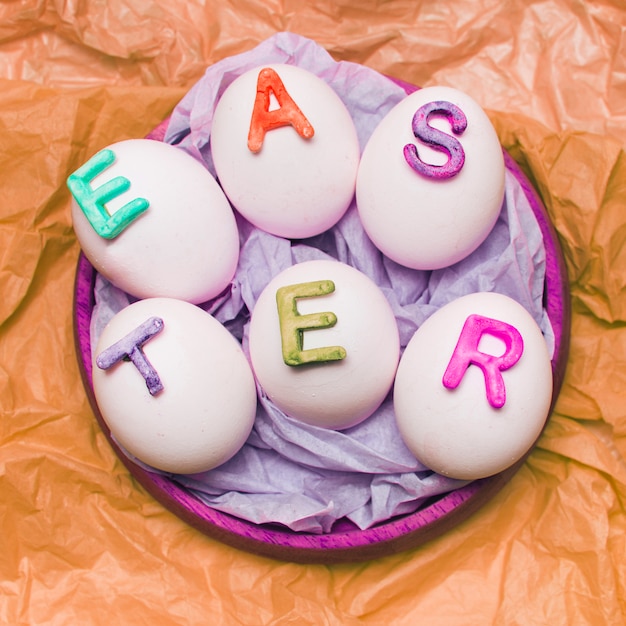 Foto gratuita uova bianche decorate con lettere sul vassoio