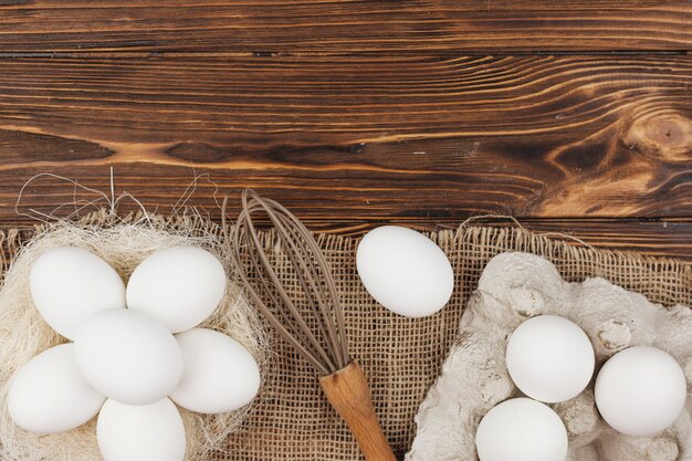 White eggs in nest and in rack with whisk on table