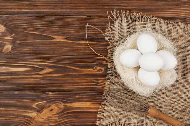 テーブルの上の泡立て器と巣の中の白い卵