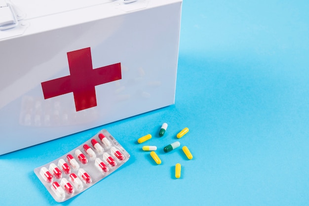 White first aid kit with colorful capsules on blue background