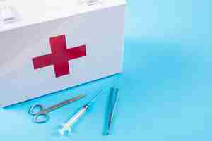 Free photo white first aid kit with scissor; syringe and tweezers on blue background