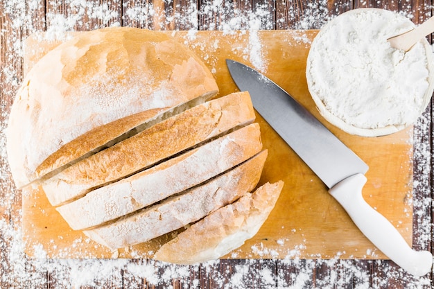 White flour spread over the bread loaf with knife on chopping board