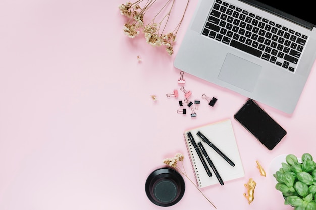 White flowers with laptop; smartphone and stationery over pink backdrop