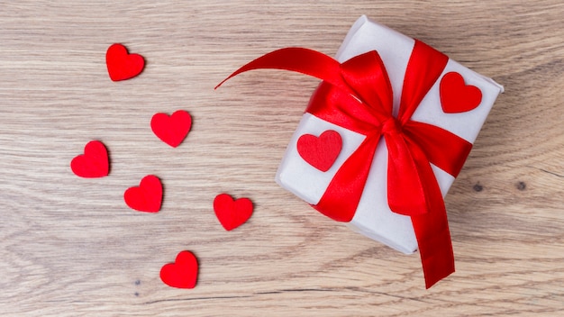 White gift box with red hearts on table 