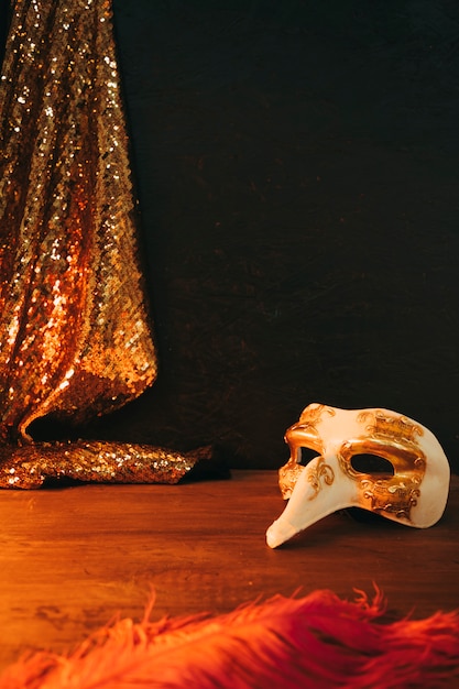 White and golden carnival mask with feather and sequins textile against black background