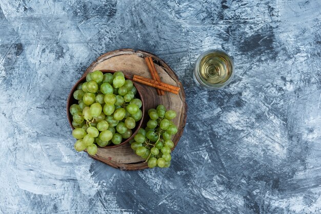 White grapes, cinnamon on a wooden board with glass of whisky top view on a dark blue marble background