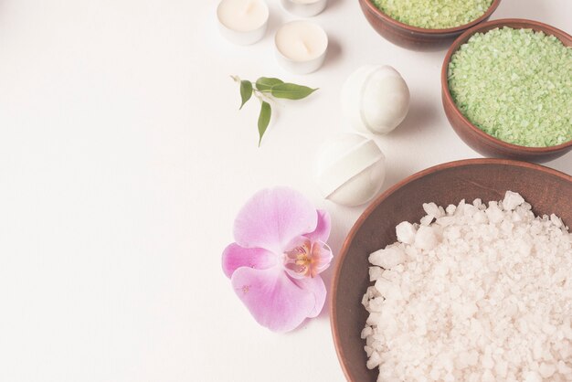 White and green spa bath salt bowl with spa bomb and orchid on white backdrop