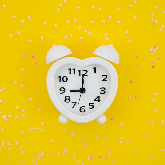 Free photo white heart shaped clock on yellow background