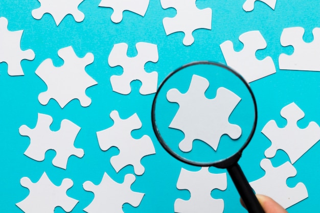 White jigsaw piece seen through magnifying glass over blue white background