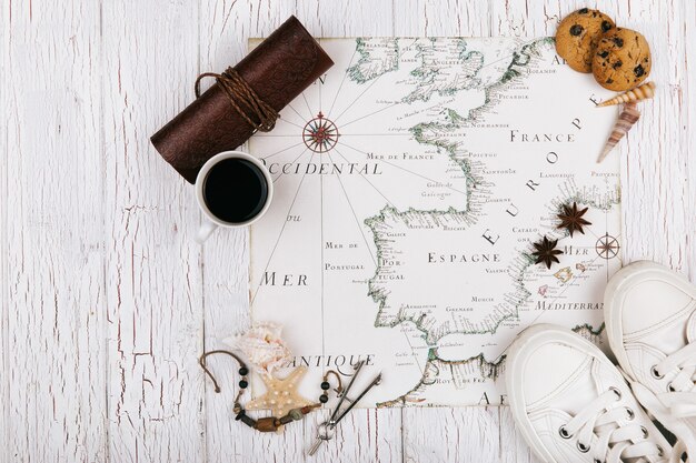 White keds, cup of coffee, cookies and sea stars stand on white map