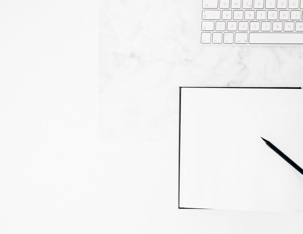 White keyboard with pencil and notebook on desk against white background