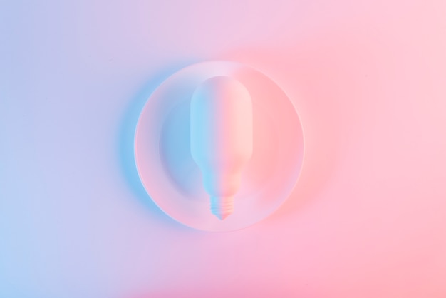 青とピンクの背景の皿の上の白い電球