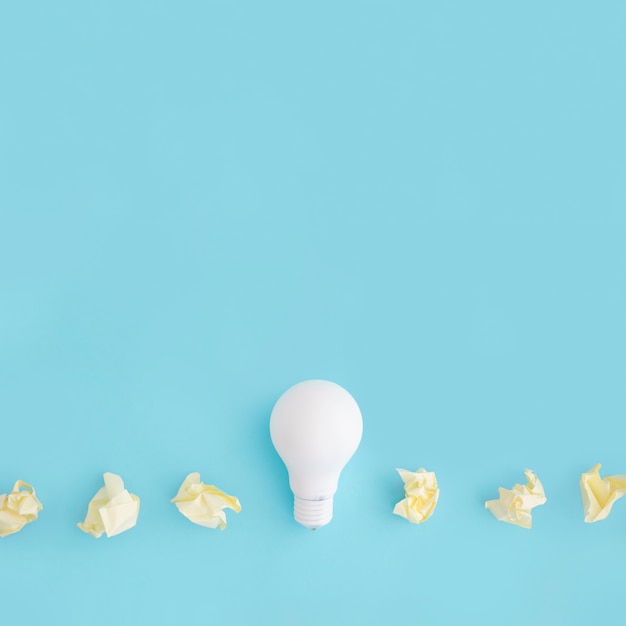 White light bulb with yellow crumpled paper on colored background
