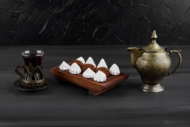 White marshmallows and cocoa pralines on a wooden platter with a glass of tea. 
