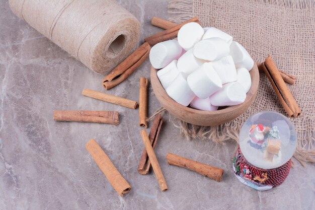 White marshmallows in a wooden cup with cinnamon sticks around.