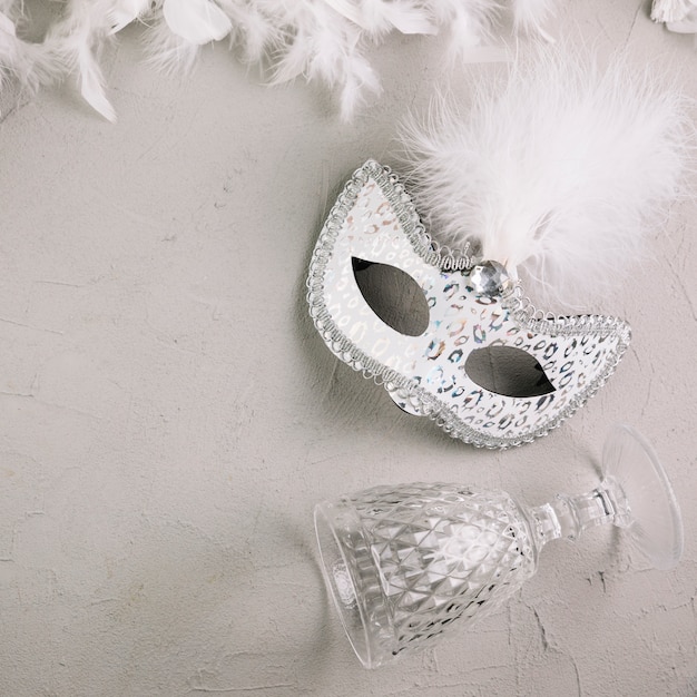 Free photo white masquerade carnival feather mask with wine glass and boa feather on concrete background