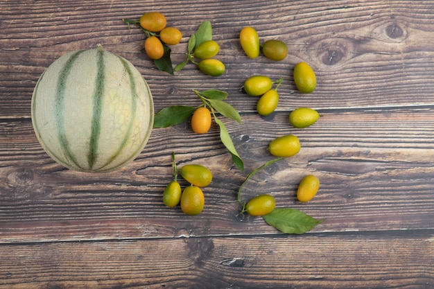 White melon and fresh kumquat fruits on wooden table.