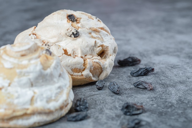 White meringue cookies with black raisines on a concrete surface.