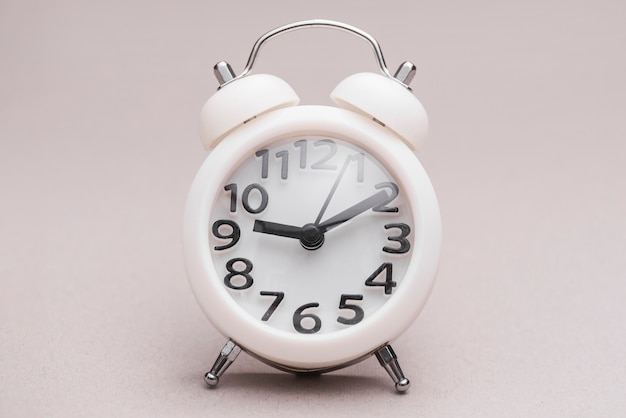 White miniature alarm clock against colored backdrop