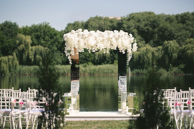 白い​花​で​飾られた​白い​鏡張り​の​結婚式​の​アーチ