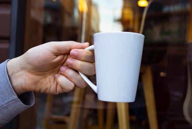 White mug held by a hand on an outdoor background