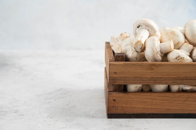 White mushrooms inside a wooden tray on a marble table.