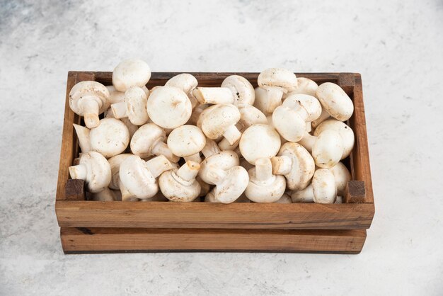 White mushrooms inside a wooden tray on a marble table.