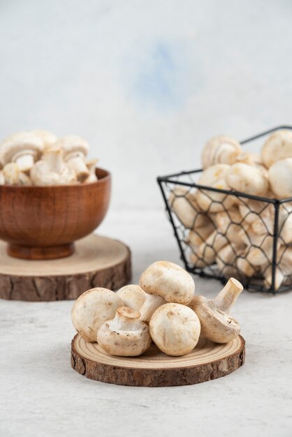 White mushrooms in a metallic basket, inside a wooden cup and on a wooden board.