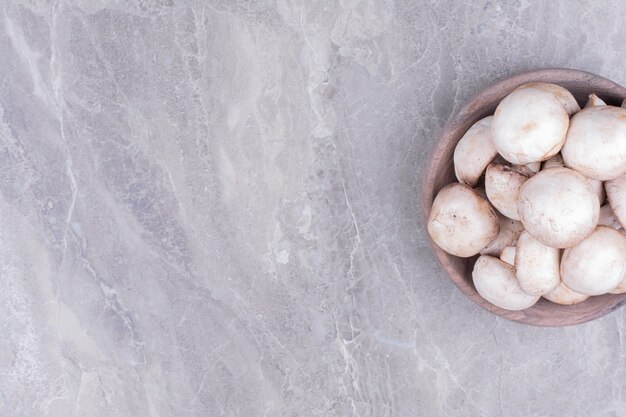 White mushrooms in a wooden cup on grey surface