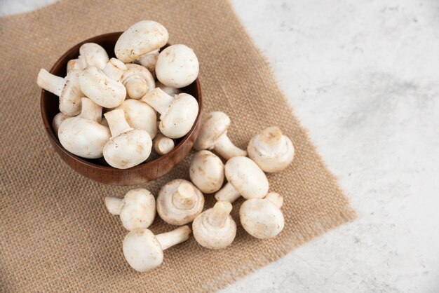 White mushrooms in a wooden cup on a piece of burlap.