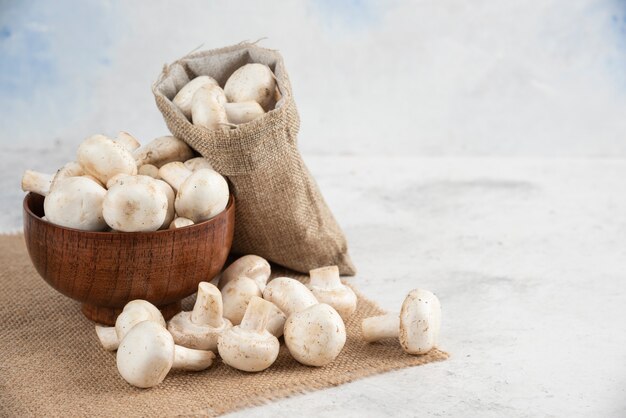 White mushrooms in a wooden cup on a piece of burlap.