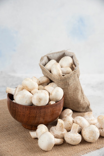 White mushrooms in a wooden cup on a piece of burlap.