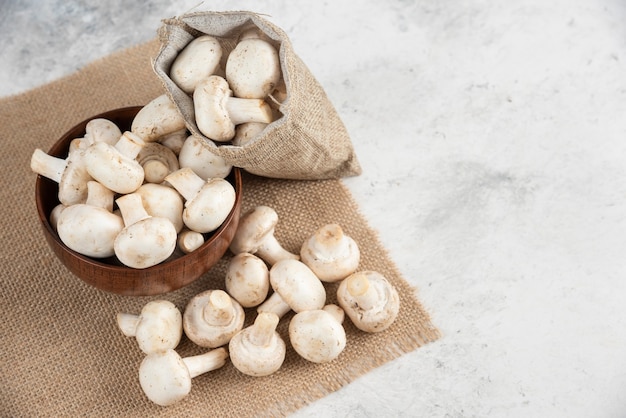 White mushrooms in a wooden cup on a piece of burlap.