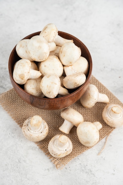 White mushrooms in a wooden cup on a piece of burlap.