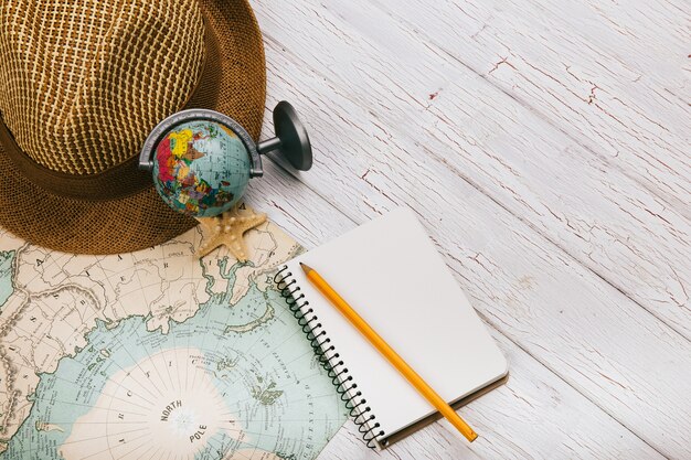 White notebook, smartphone, seastar, globe and hat lie on yellow map