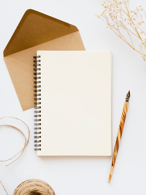 White notebook with a wooden  nib on a pale brown envelope with a brown thread and a branch on a white background