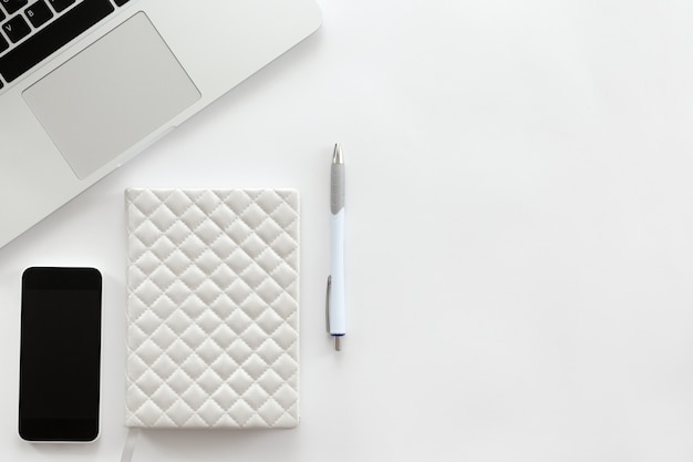 White office desk with a part of laptop, mobile phone, pen