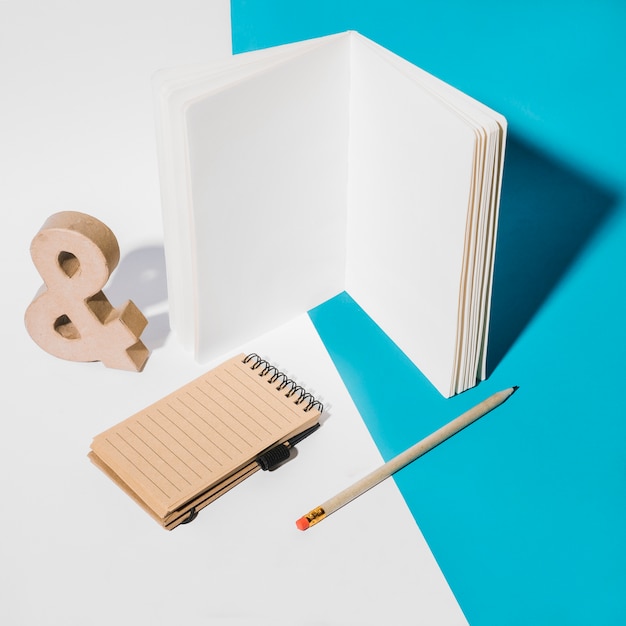 White page notebook; spiral notepad; ampersand symbol and pencil on dual background