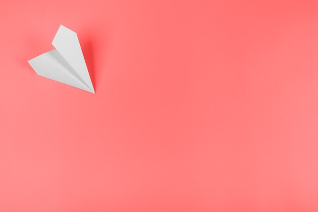 White paper airplane on the corner of the coral background