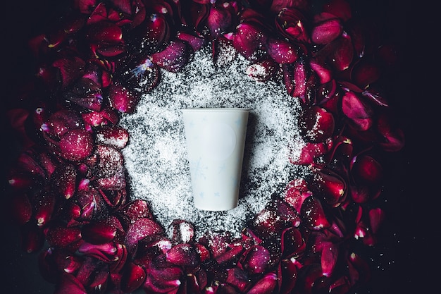 White paper cup lies in white powder in the circle of red rose petals