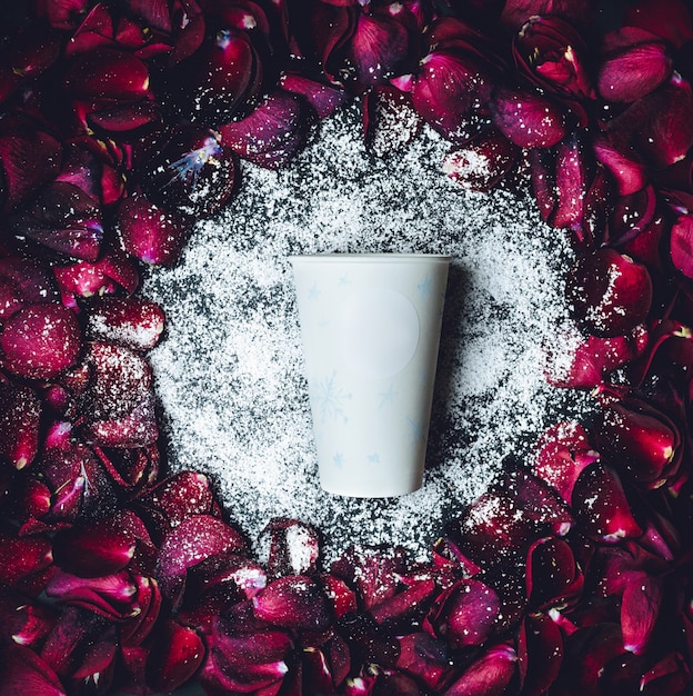 白い紙のカップは、赤いバラの花びらの円の中に白い粉の中にある