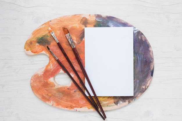 Free photo white paper on palette with paint brushes