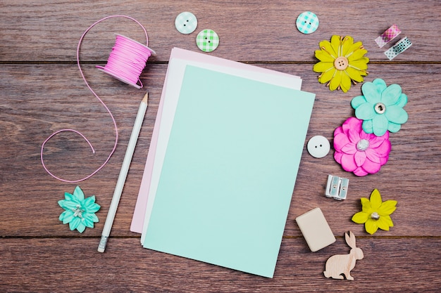 White pencils; buttons; colorful flowers and pink spool on wooden table